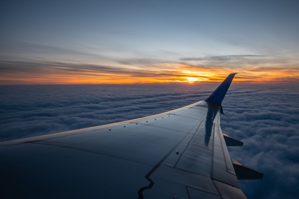 An airliner wing above a layer of cloud at sunset